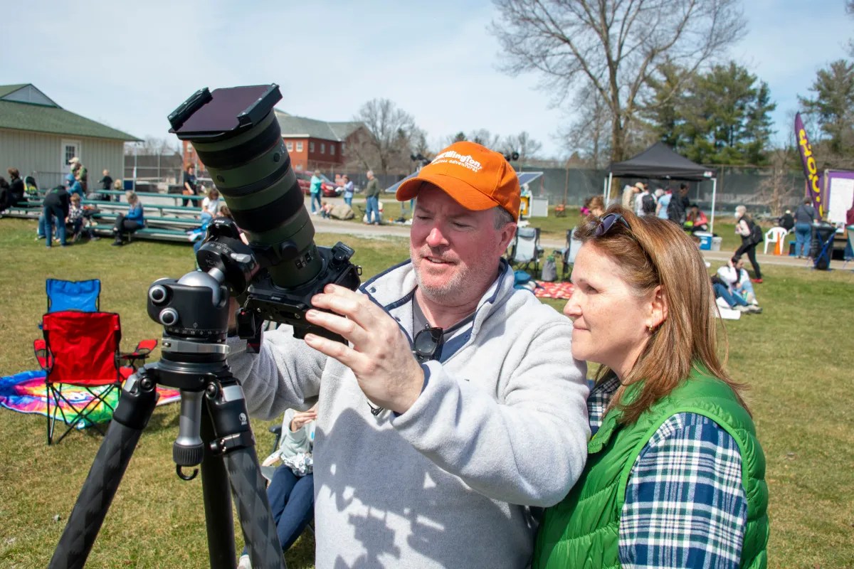 A man and a woman observing through a telescope set up outdoors during daytime.