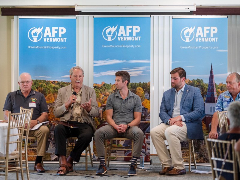 Five men are seated on a panel in front of AFP Vermont banners, with one man speaking into a microphone during an event.