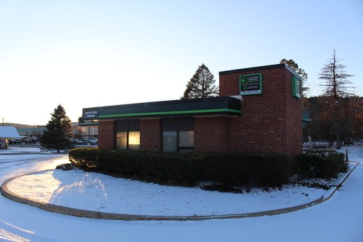 Small brick building with a snow-covered ground, surrounded by a few trees and bushes. A sunset sky in the background.
