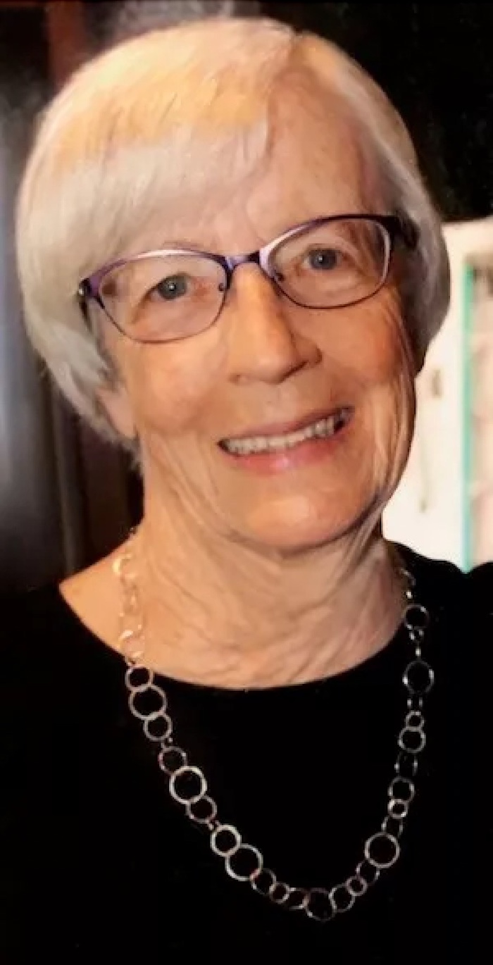 A woman with short hair and glasses, wearing a black top and a silver chain necklace, smiling at the camera.