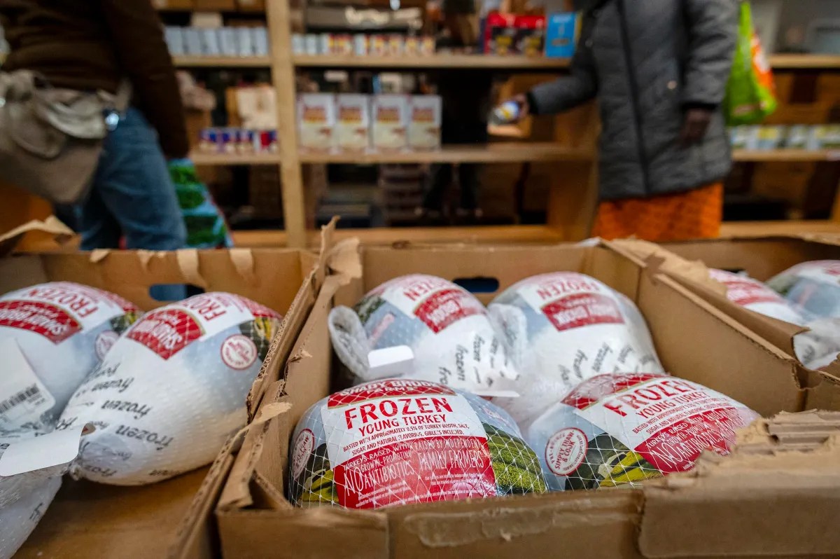 Boxes of frozen turkeys labeled "Young Turkey" in a grocery store aisle, with people browsing in the background.