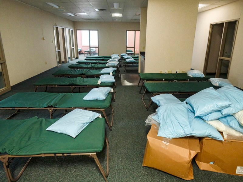 A makeshift dormitory setup with rows of simple cots and bedding in an indoor facility.