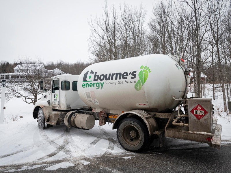 A Bourne's Energy truck parked on a snowy road near bare trees and a house in the background.