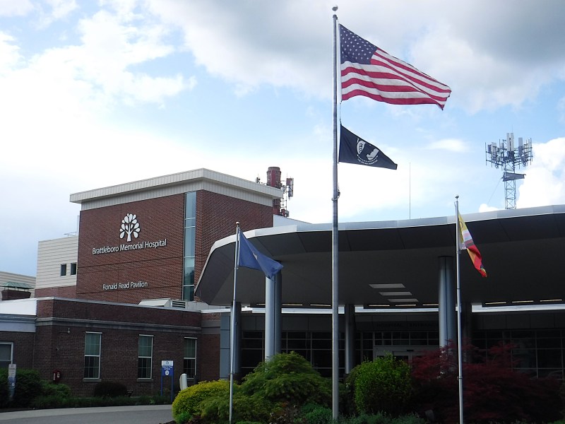 Brattleboro Memorial Hospital exterior with three flagpoles, including the American flag, in front of the building under a partly cloudy sky.