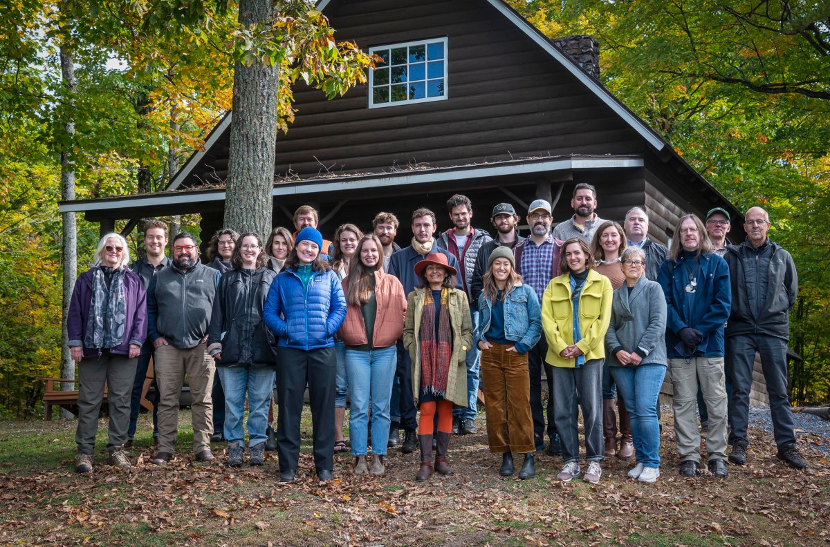 A group of people standing in front of a wooden cabin surrounded by trees.