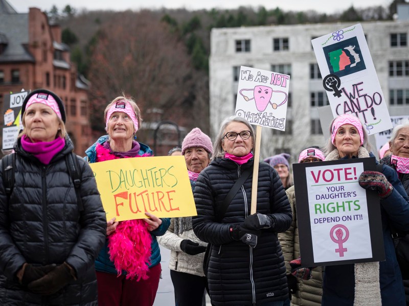 A group of people, mostly women, stand outdoors holding signs advocating for women's and daughters' rights.