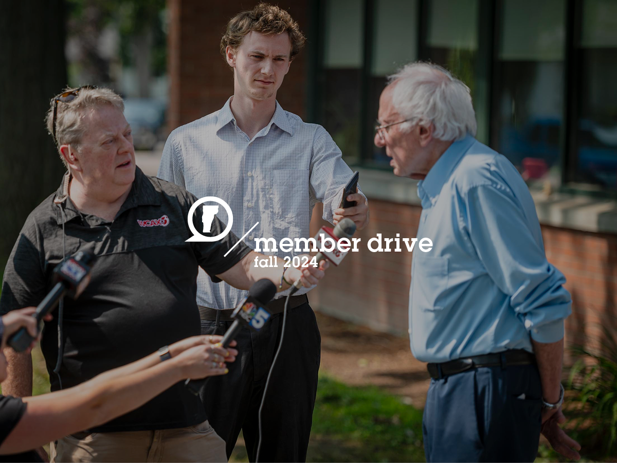A man in a light blue shirt is speaking outside while three people hold microphones toward him. Text overlays the image, reading "member drive fall 2024.
